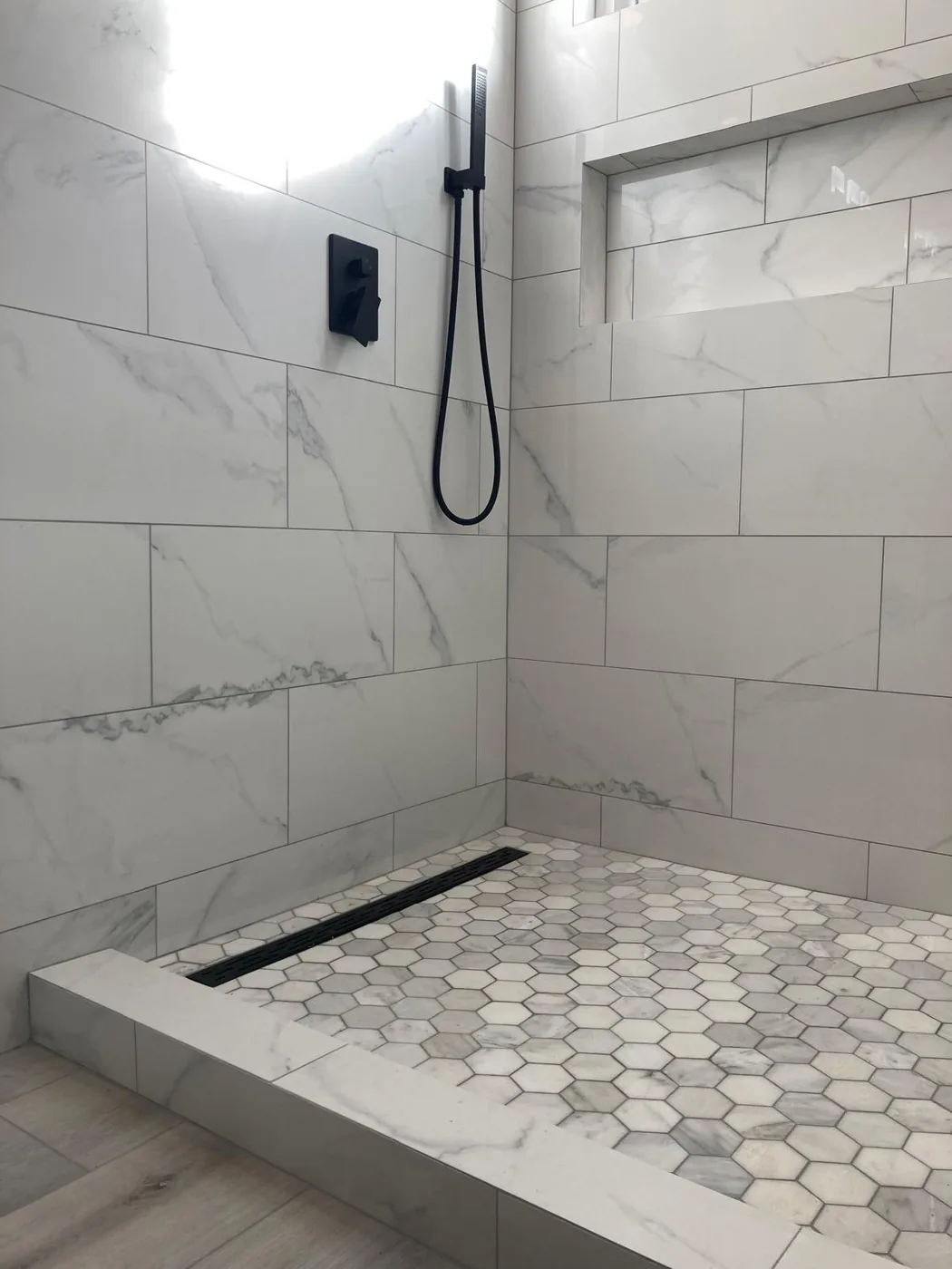 Walk-in shower with marble-look tile, hexagon mosaic floor and black linear drain